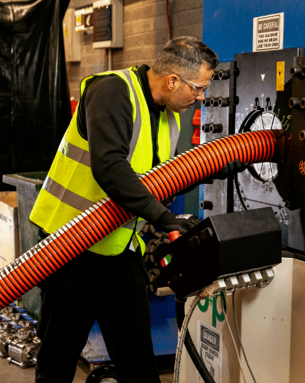 A man wearing a yellow vest inspecting quality of hose assemblies.